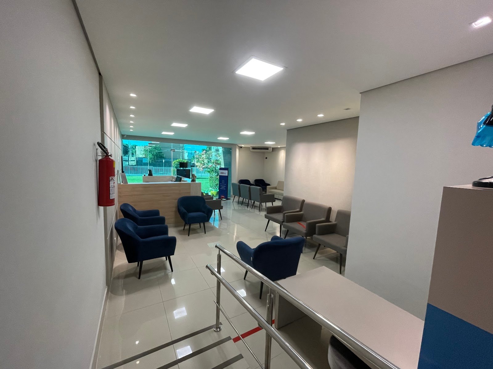Recepção ampla e iluminada, com poltronas azuis e cinzas e piso claro.