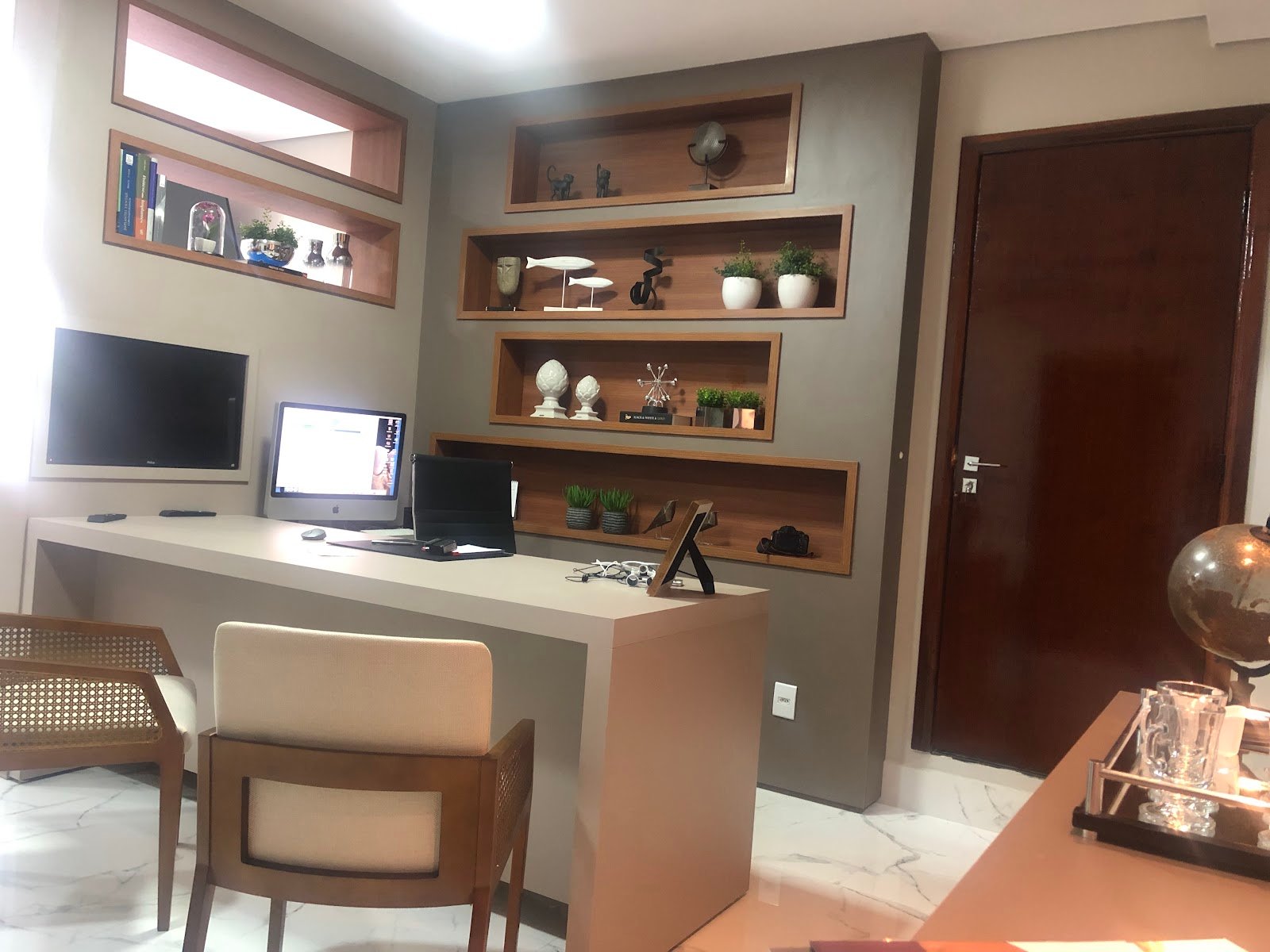 Consultório com escrivaninha, nichos de madeira decorados e piso de mármore.